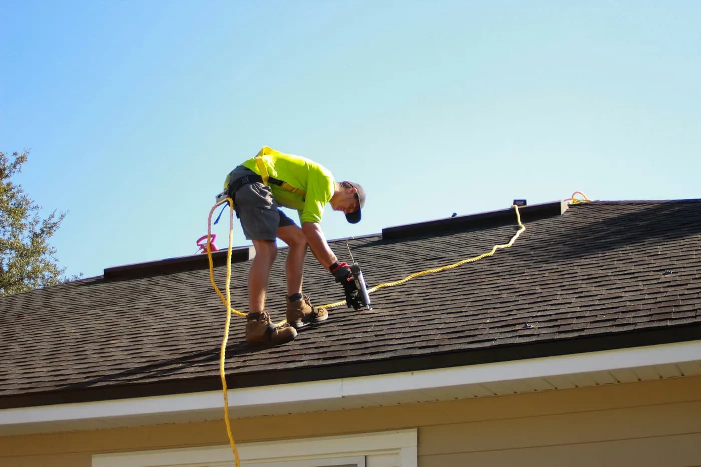 A roofer wearing a safety harness working on an asphalt shingle roof