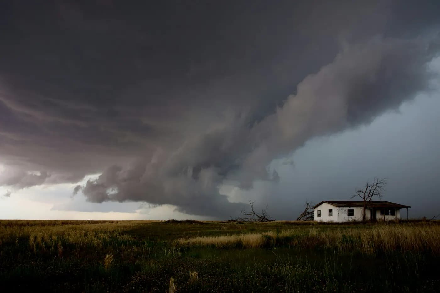 A large storm cloud building over a single house in open country