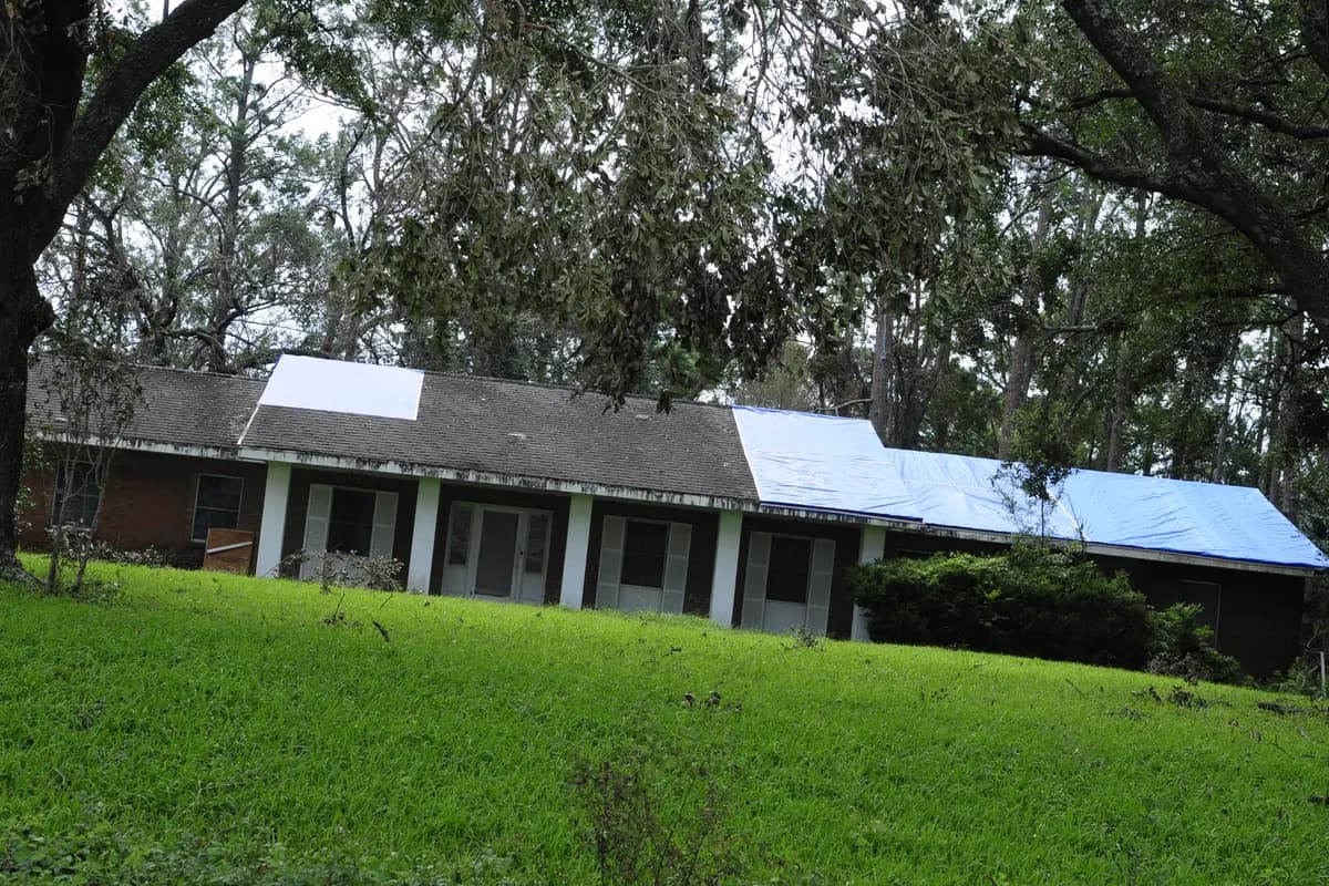 A blue tarp secured over part of a damaged house roof as temporary protection after a storm