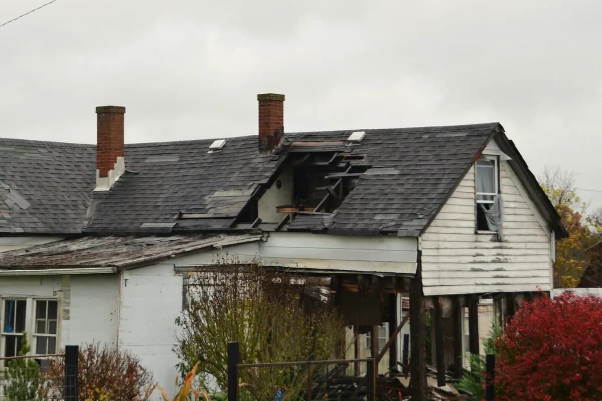 A house whose shingle roof has a section torn open down to the framing