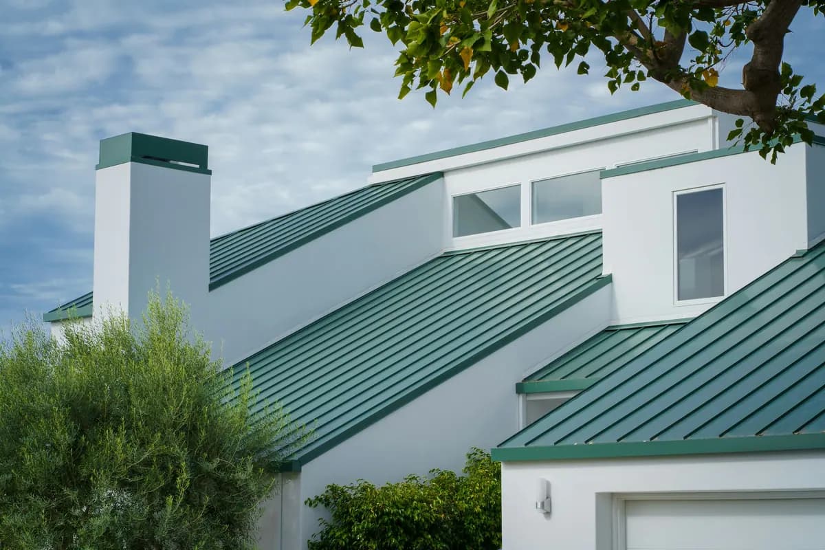 A white house with green standing-seam metal roofs over several wings
